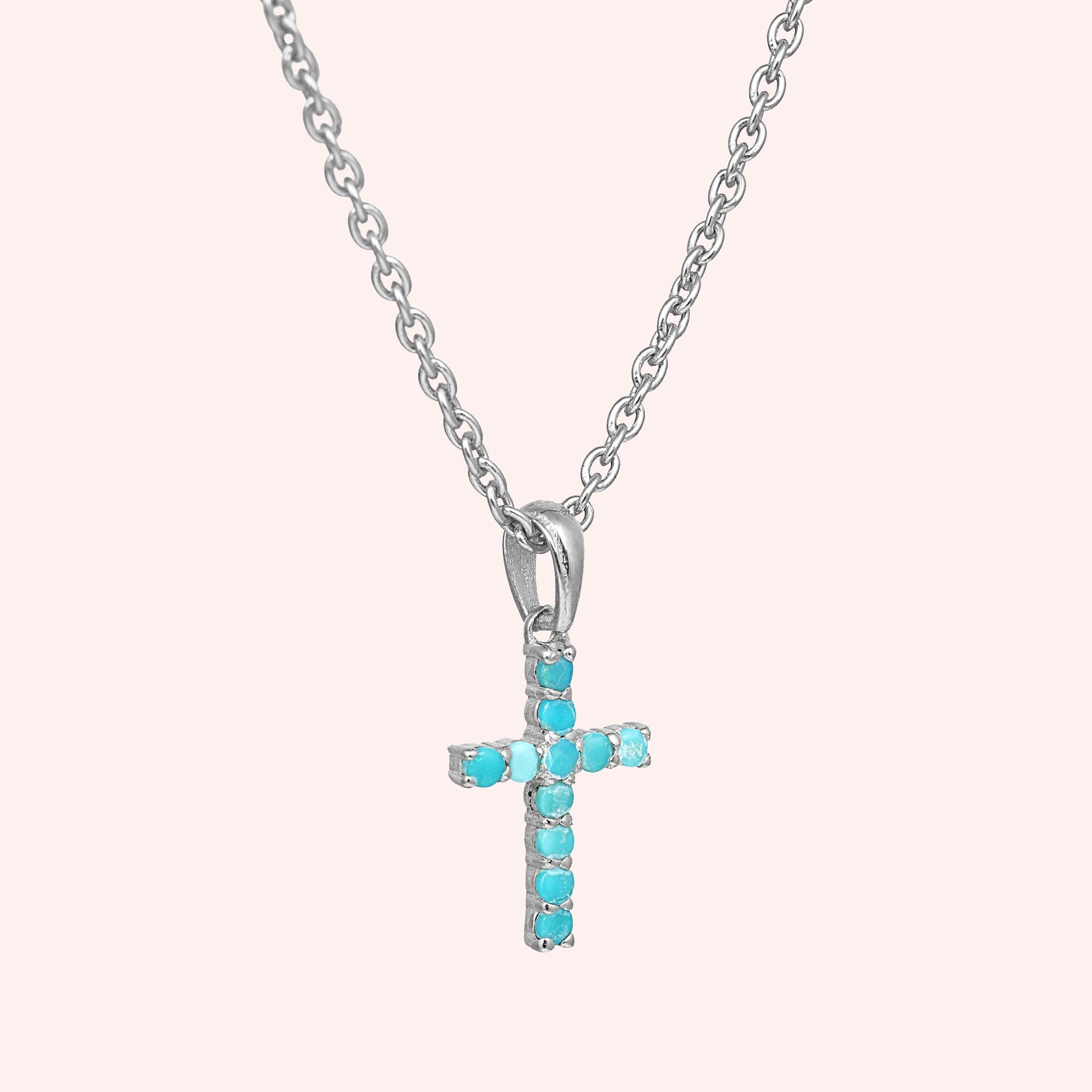 A front side angle of a sterling silver cross pendant necklace with turquoise cross necklace stones over a light pink backdrop