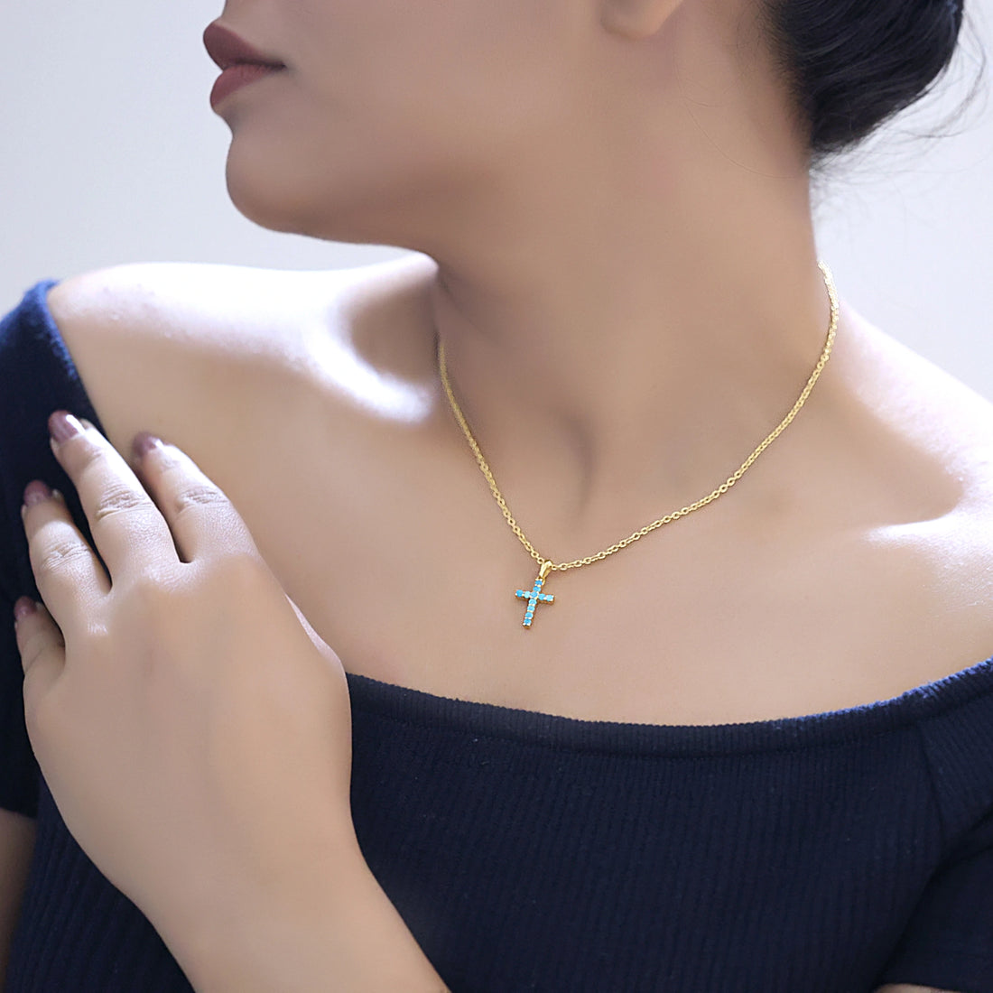 Front angle view of sterling silver cross pendant necklace and turquoise cross necklace on a white textured fabric background