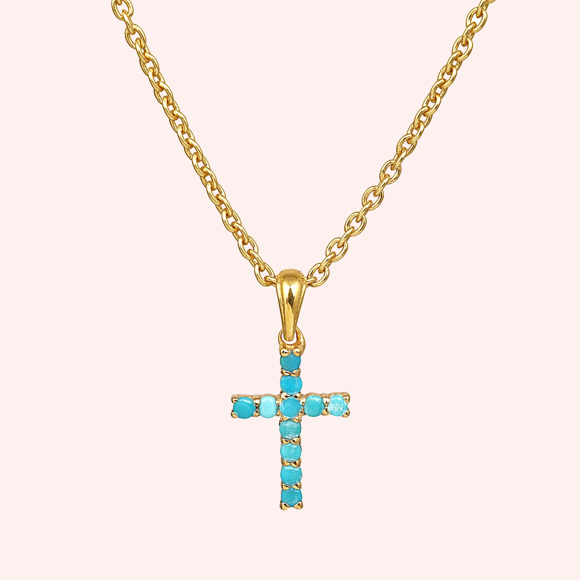 A gold plated sterling silver cross pendant necklace and turquoise cross necklace at a front angle view on a light pink background