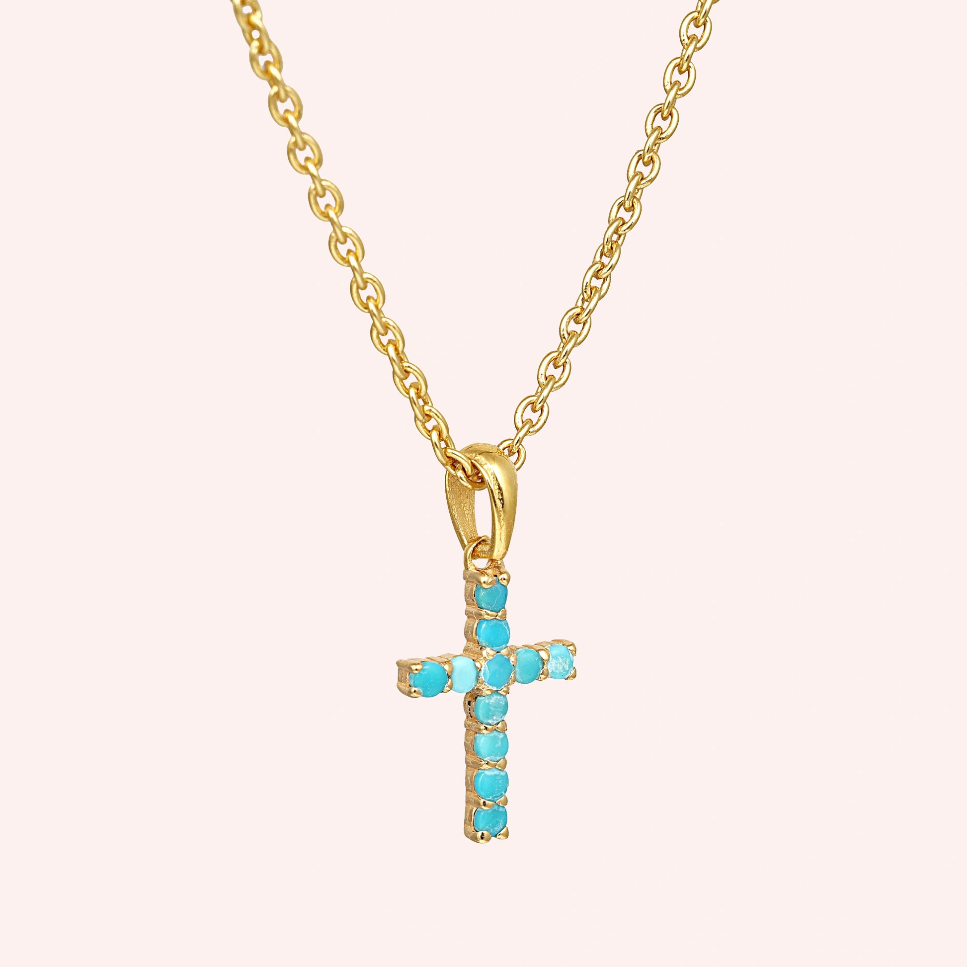 Gold plated sterling silver cross pendant necklace with a turquoise cross necklace at a side angle view on a pink background