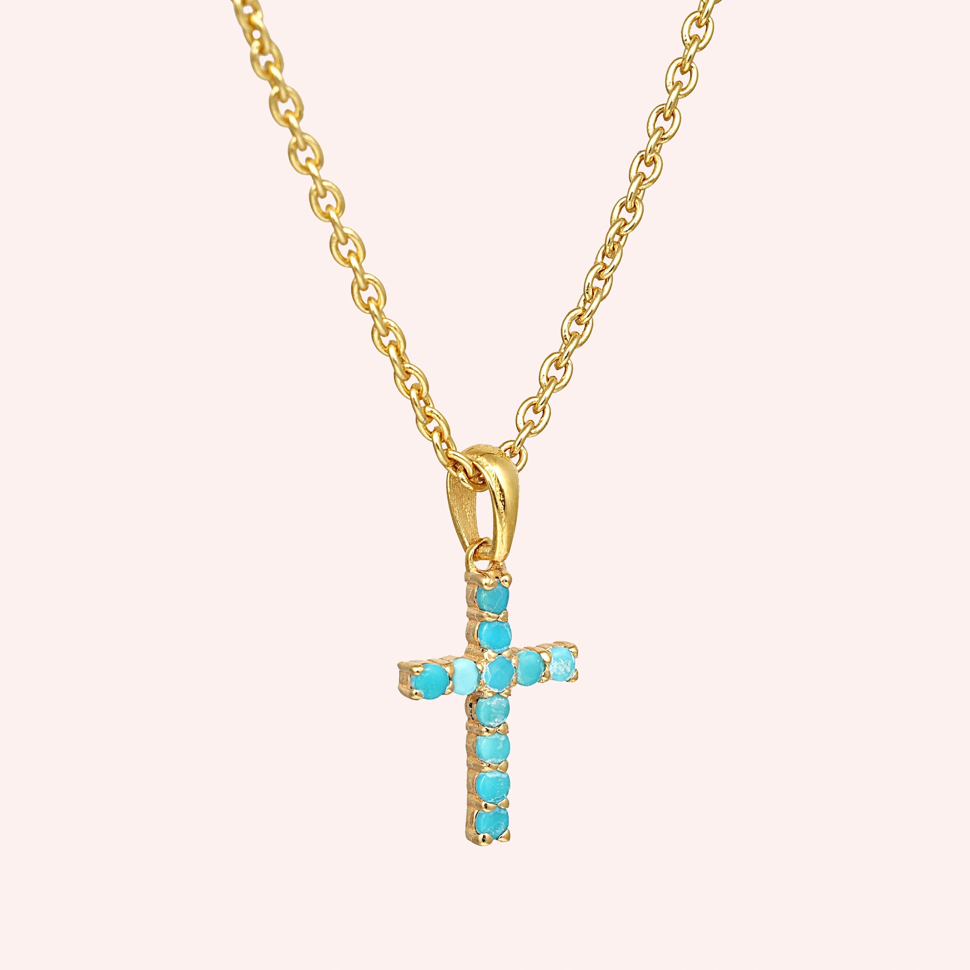 Gold plated sterling silver cross pendant necklace with a turquoise cross necklace at a side angle view on a pink background