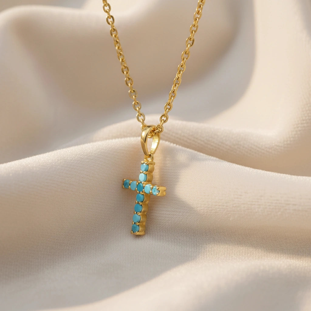 A side angle of gold plated sterling silver cross pendant necklace and turquoise cross necklace on white textured fabric
