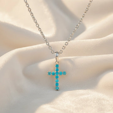 Front angle view of sterling silver cross pendant necklace and turquoise cross necklace on a white textured fabric background