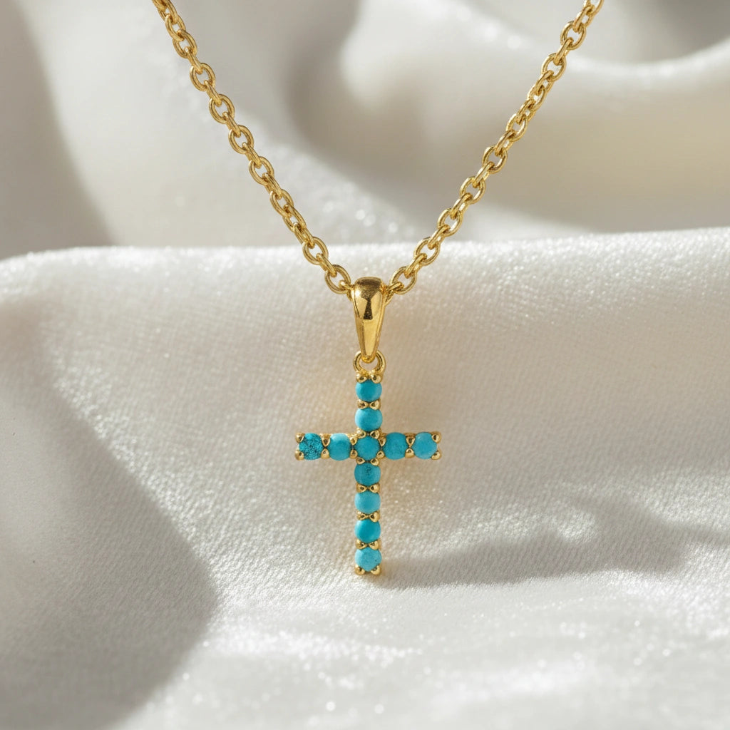 A front angle of gold plated sterling silver cross pendant necklace and a turquoise cross necklace on white textured fabric