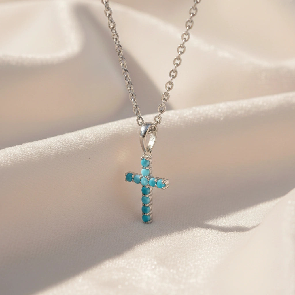 Side angle view of sterling silver cross pendant necklace and turquoise cross necklace on a white textured fabric background